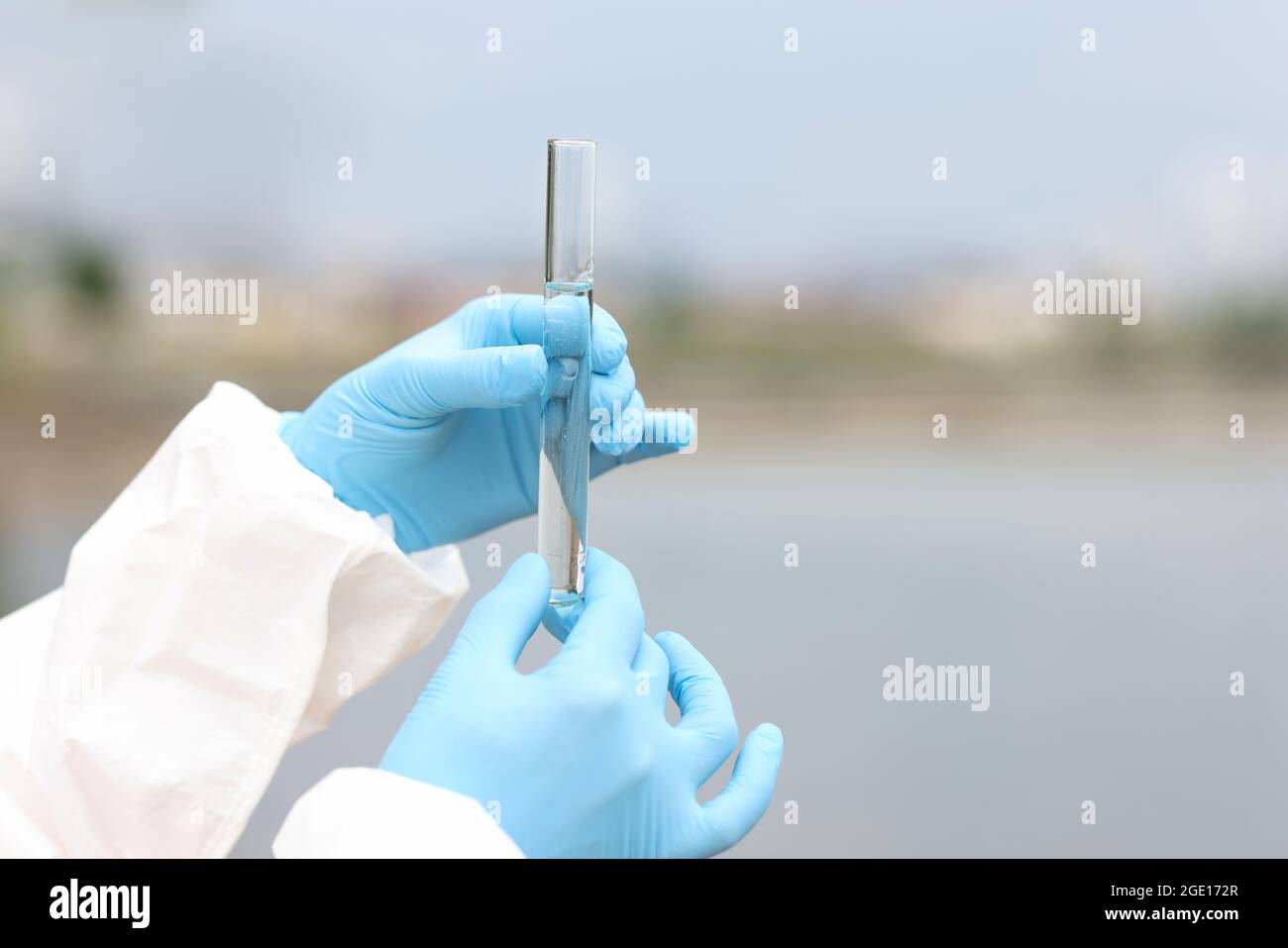 Scienziato in guanti di gomma che tengono una provetta con un campione d'acqua proveniente dalla chiocciatura del fiume Foto Stock