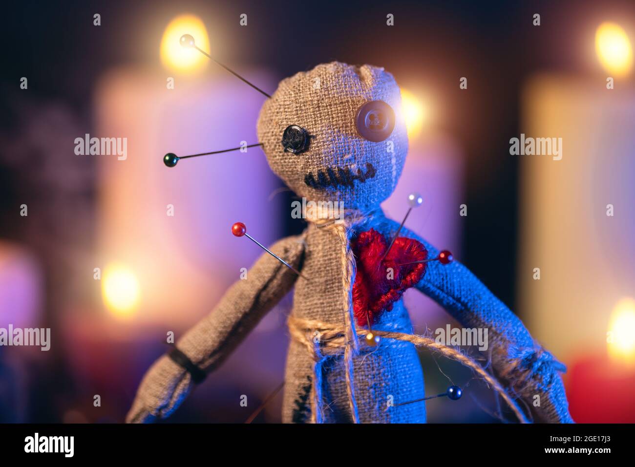 Voodoo bambola chiodata con aghi con cuore piercato rosso strag sullo sfondo di candele brucianti. Rituale esoterico magico e inquietante. Foto Stock