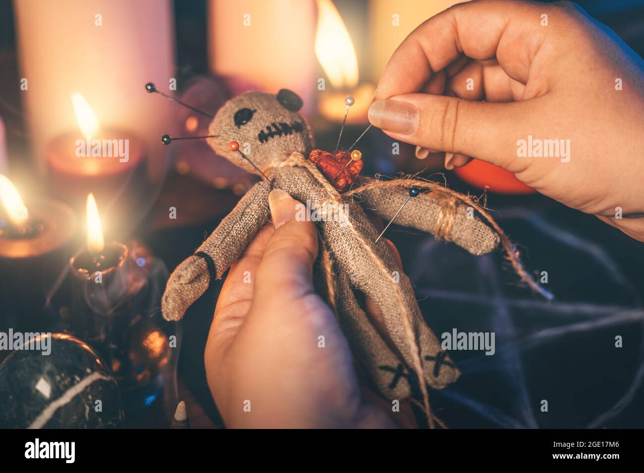Le mani femminili attaccano gli aghi nel corpo della bambola voodoo RAG. La strega esegue una stregoneria sinistra. Concetto di rituali occulti, esoterici e mistici. Foto Stock