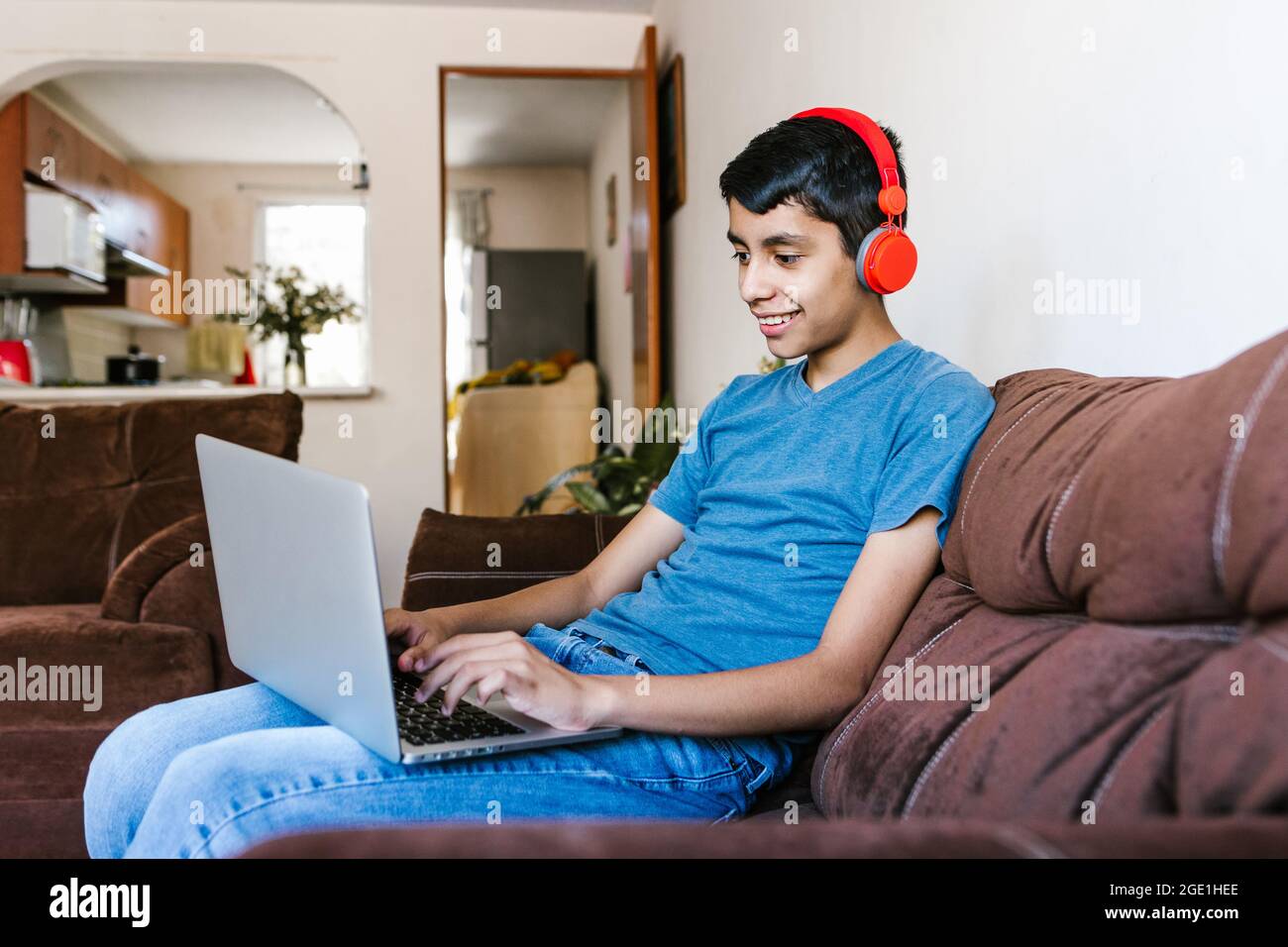 Adolescente ispanico con cuffie che ascolta la musica mentre usi un computer portatile a casa in America Latina Foto Stock