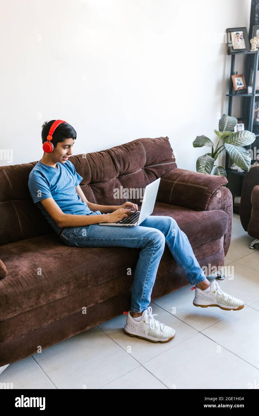 Adolescente ispanico con le cuffie seduti sul divano mentre si usa il computer portatile a casa in America Latina Foto Stock