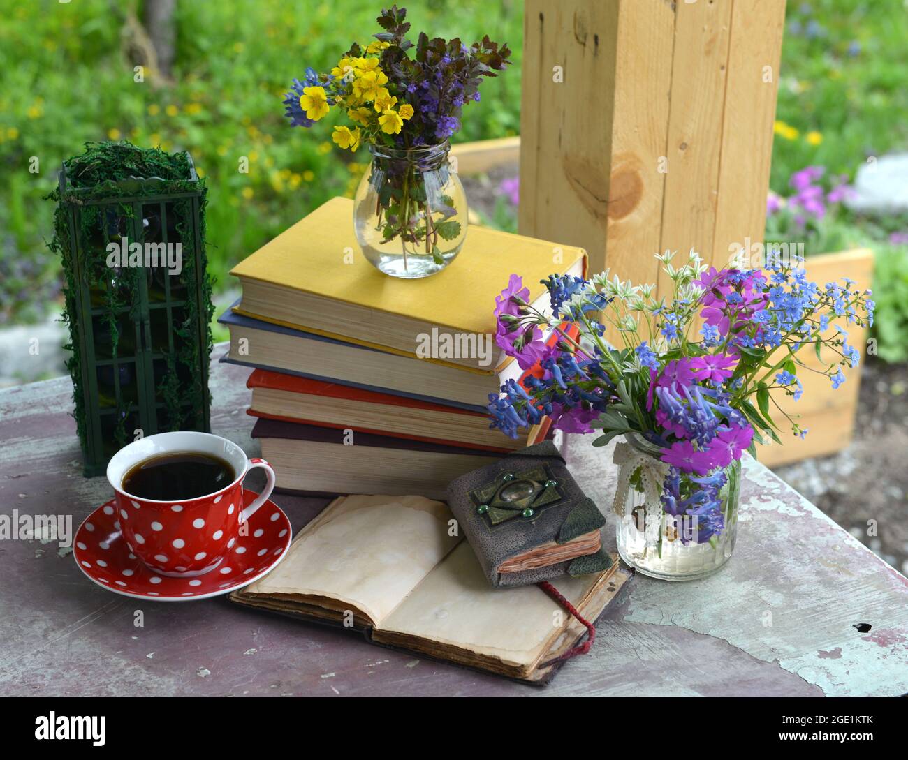 Ancora vita con mazzo di fiori primaverili, libri, tazza di tè e diario aperto sul tavolo. Concetto romantico d'epoca all'esterno in giardino Foto Stock