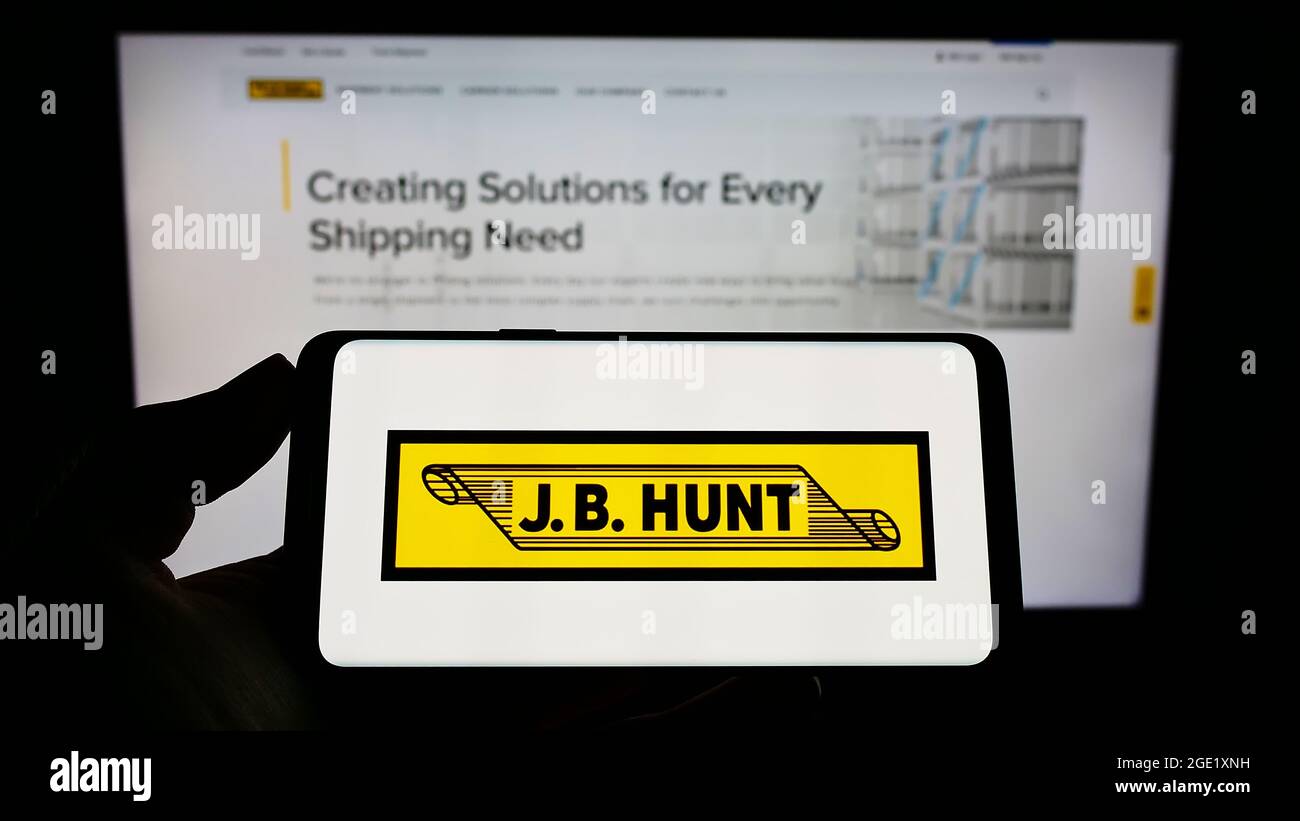 Persona che tiene il cellulare con il logo della società logistica J.B. Hunt Transport Services Inc. Sullo schermo davanti alla pagina Web. Mettere a fuoco il display del telefono. Foto Stock