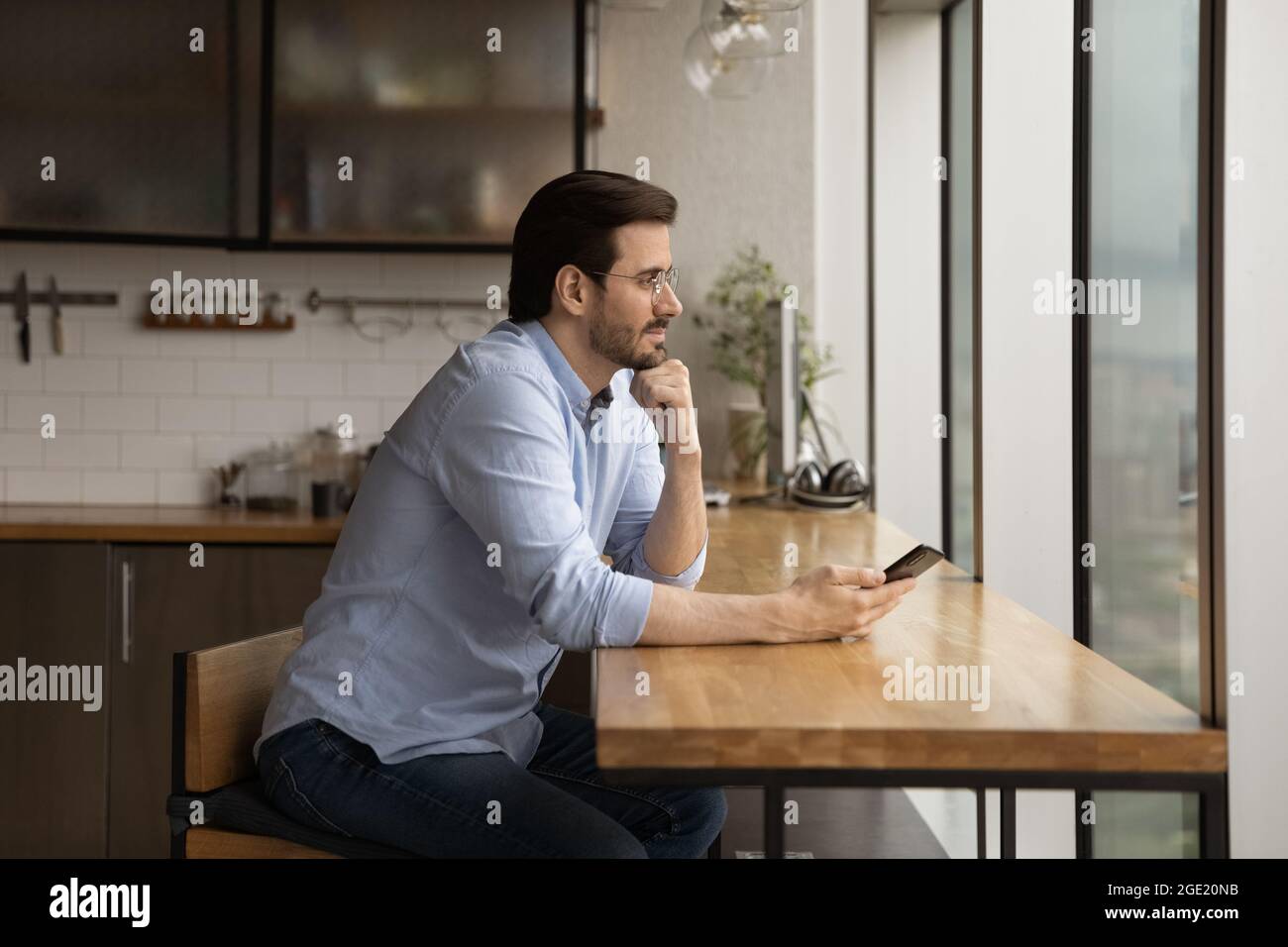 Uomo d'affari tranquillo sedersi in ufficio cucina tenere smartphone daydreaming Foto Stock