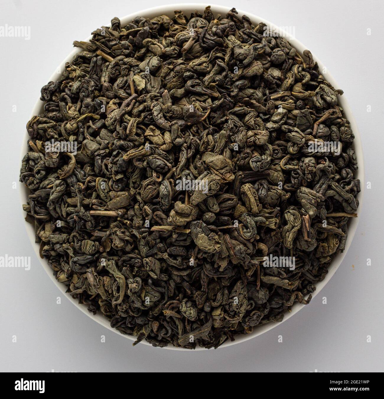 Foglie di tè verde Gunpowder cinese essiccato in una ciotola, su sfondo bianco Foto Stock