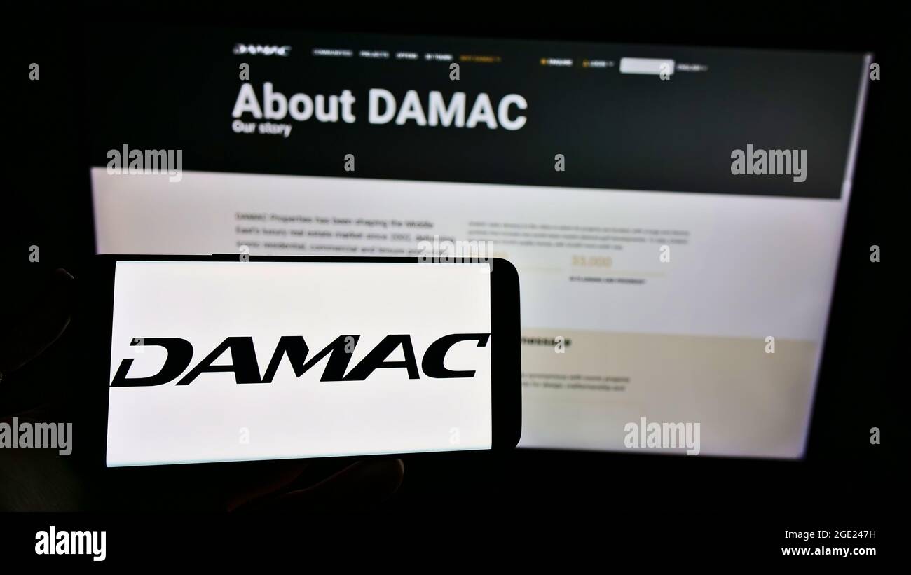 Persona titolare smartphone con logo della società immobiliare Emirati DAMAC Proprietà sullo schermo di fronte al sito web. Mettere a fuoco il display del telefono. Foto Stock