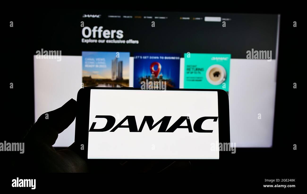 Persona titolare cellulare con logo della società immobiliare Emirati DAMAC Proprietà sullo schermo di fronte alla pagina web aziendale. Mettere a fuoco il display del telefono. Foto Stock
