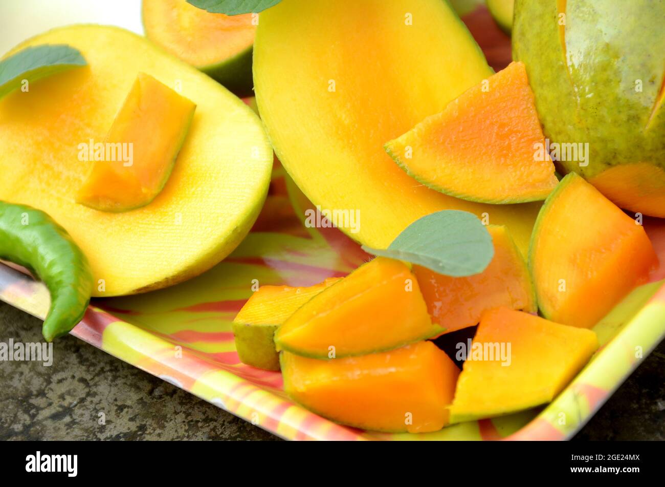 chiuda la frutta di mango giallo verde matura tagliata a fette con le foglie di menta verde e fredda nel vassoio sopra fuori di fuoco sfondo marrone grigio. Foto Stock