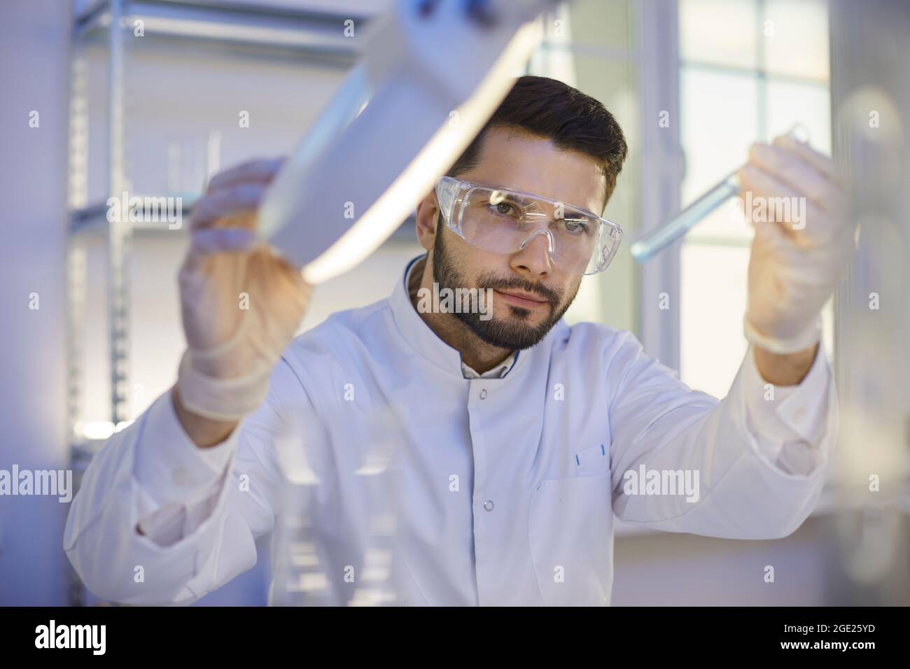 Ricercatore che guarda con la provetta di liquido chimico sotto lampada in laboratorio Foto Stock