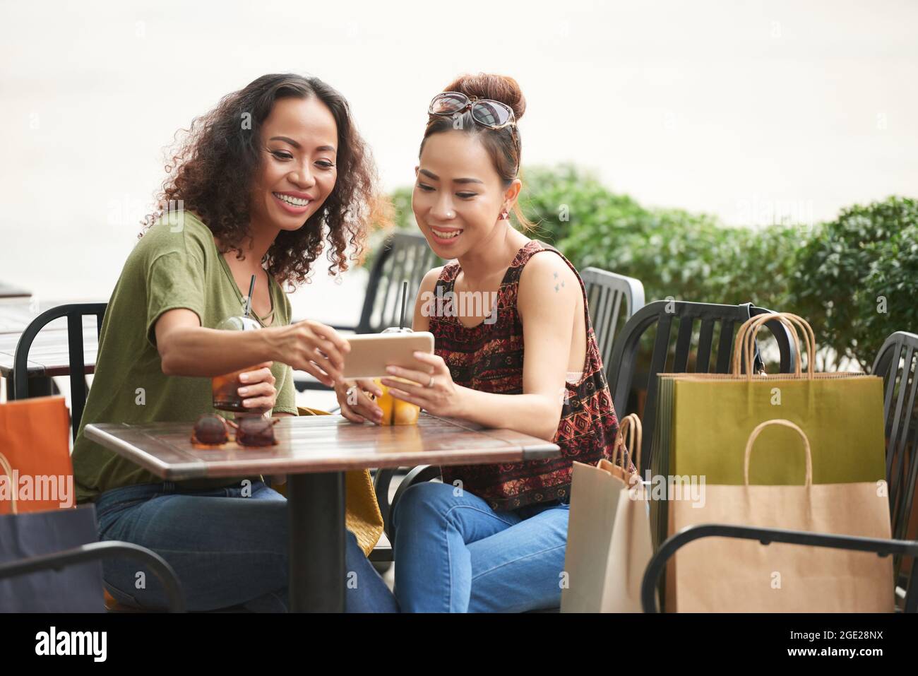 Giovane donna sorridente che mostra le foto sullo smartphone ad un amico quando si incontrano al tavolo del caffè Foto Stock