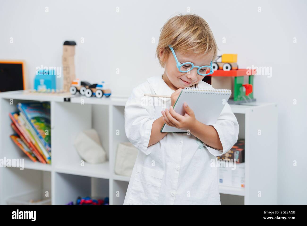Bambino felice che gioca un medico, indossando occhiali giocattolo e accappatoio bianco Foto Stock