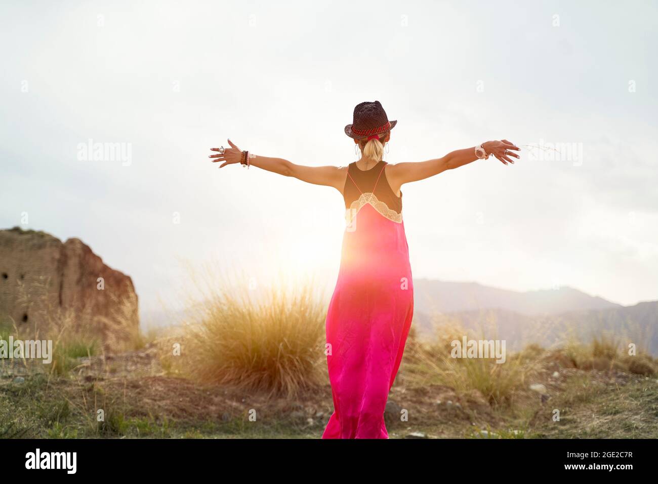 vista posteriore di una giovane donna asiatica in abito rosso che abbraccia la luce del sole del mattino in una zona di montagna deserta Foto Stock
