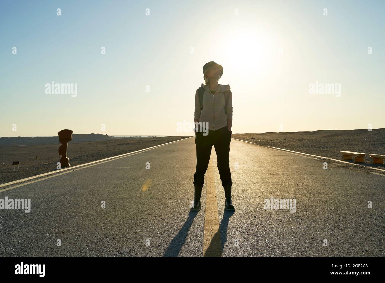donna asiatica viaggiatore zaino in spalla in piedi nel mezzo di una strada nel deserto di gobi al tramonto Foto Stock