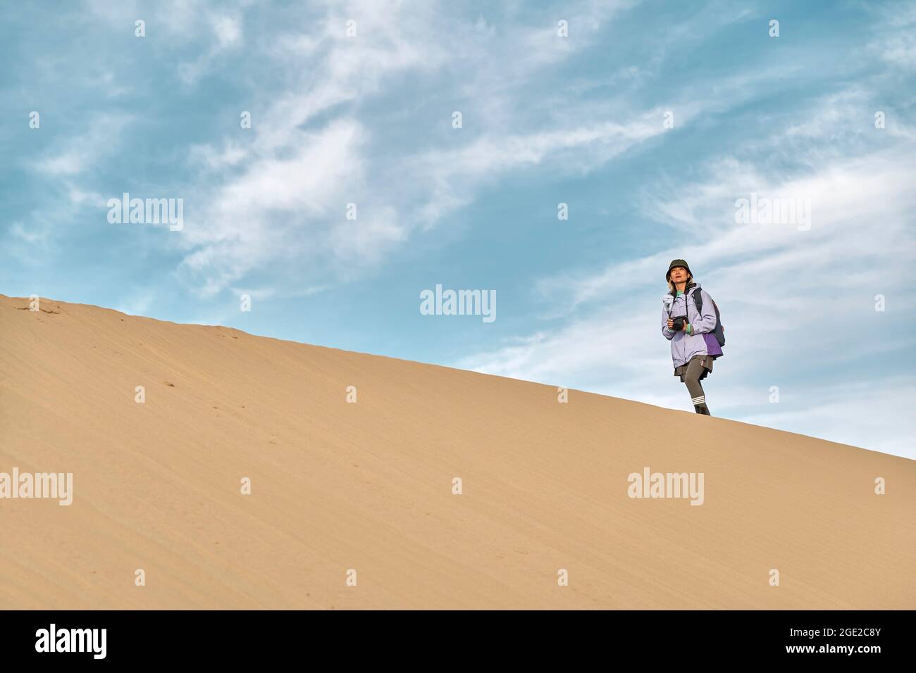 donna asiatica fotografo camminare sulla cresta di una duna di sabbia guardando la vista Foto Stock