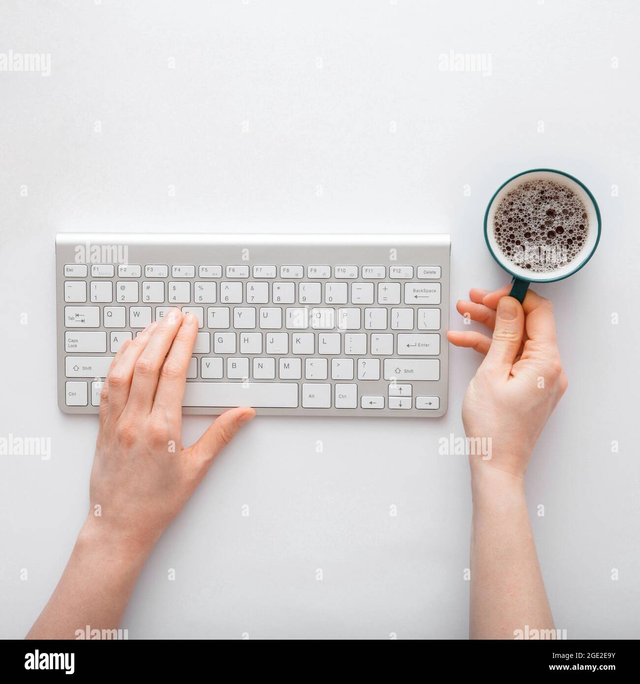 Donna che scrive sulla tastiera del computer e beve caffè sul posto di lavoro. scrivania da lavoro con le mani femminili su sfondo bianco. Foto Stock