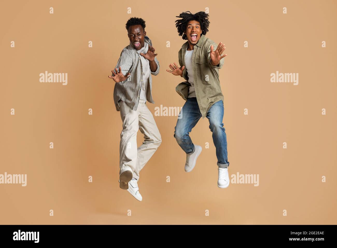 Due allegri ed emotivi African American Guys saltano sopra Beige Studio background Foto Stock