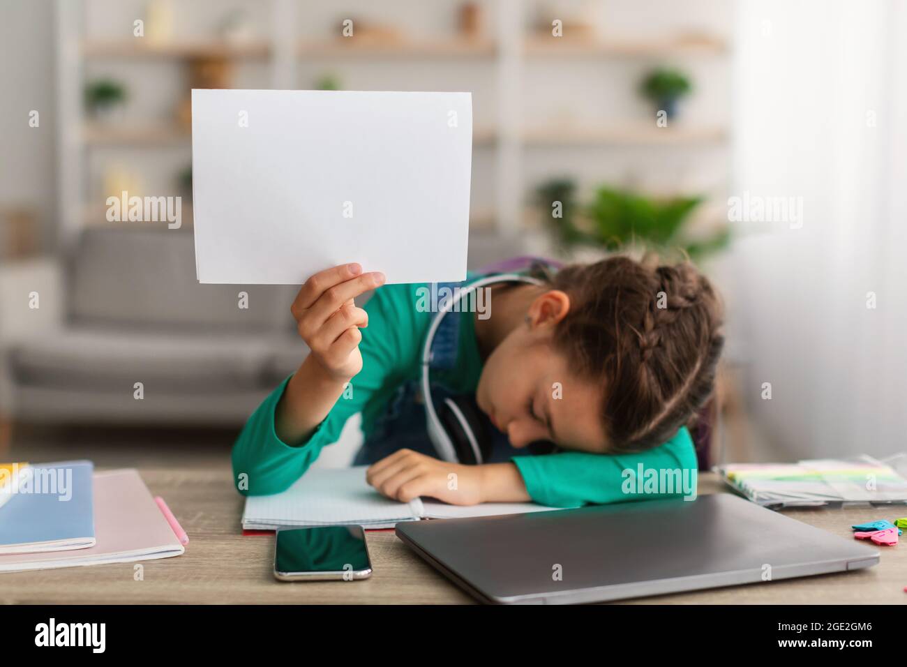 Ragazza stanca della scuola che dorme al tavolo che tiene carta Foto Stock