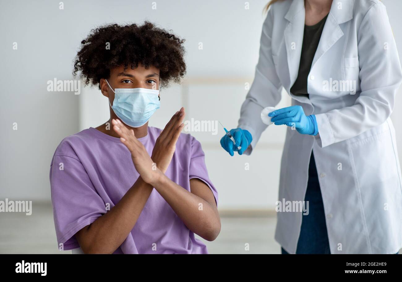 Teen afroamericano in maschera di faccia che impedisce al medico di fare il vaccino del covid, essendo contro l'immunizzazione del coronavirus Foto Stock