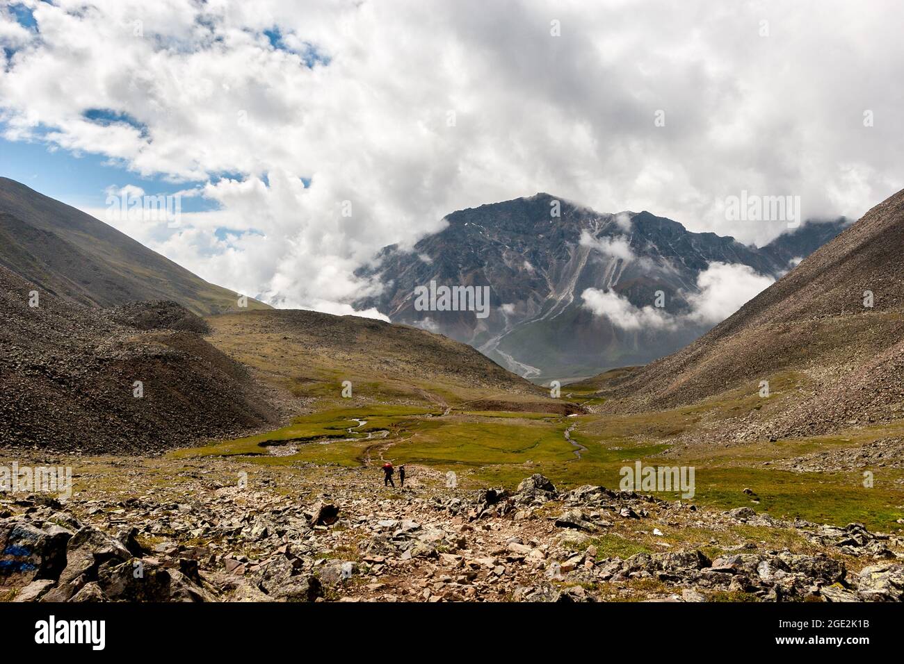 Valle di montagna con un passaggio tra le montagne e una grande montagna alla fine. Nuvole basse sulla montagna. Molti turisti vanno lungo il trai Foto Stock