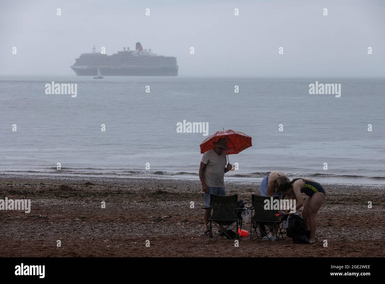 I vacanzieri hanno coraggioso gli elementi di Goodrington North Beach a Paignton, Devon, colpiti da docce tuose che costringono alcuni turisti a correre per coprire, Regno Unito. Foto Stock