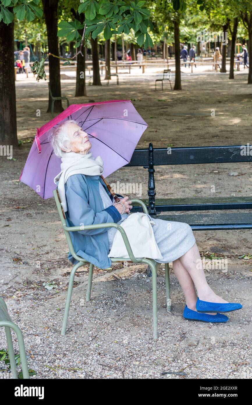 Signora che riposa sotto un ombrello viola, seduto su una sedia nel Jardins du Luxembourg a Parigi Foto Stock