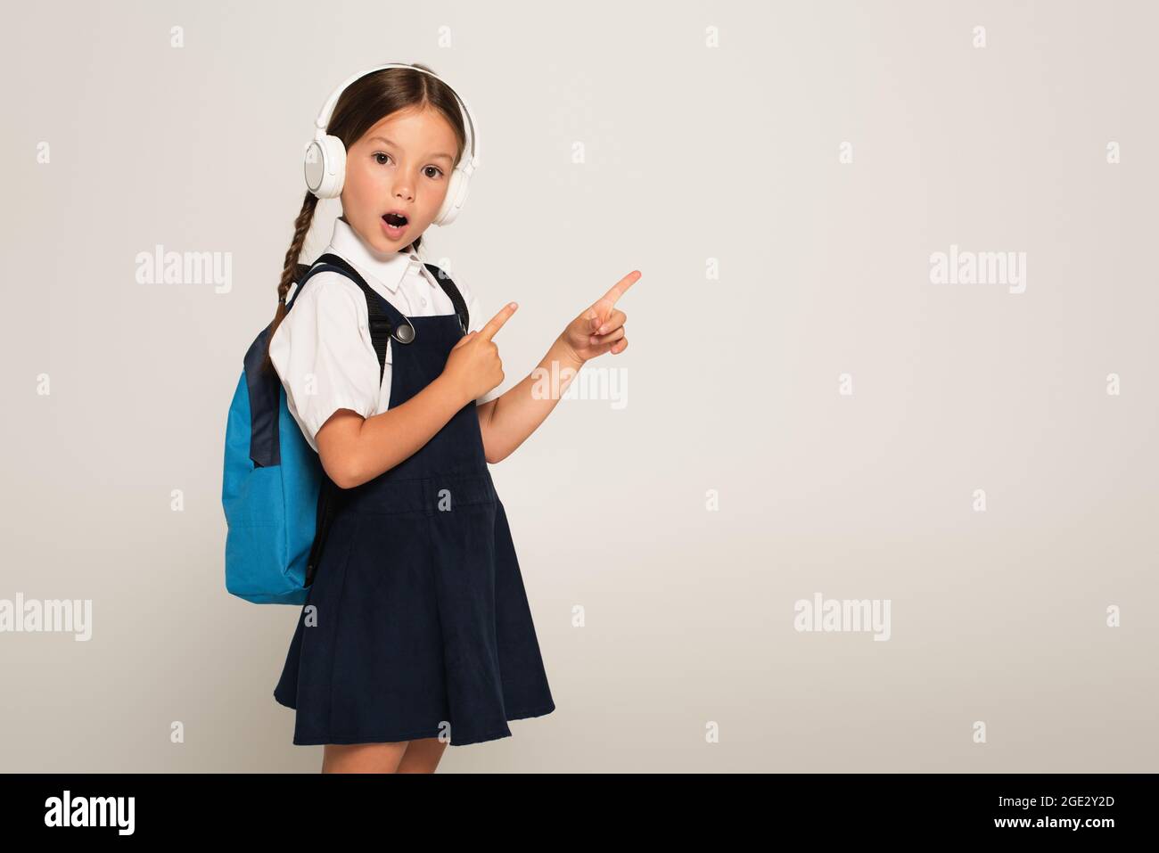 stupito scolaretto con le cuffie che puntano con le dita isolate su grigio Foto Stock