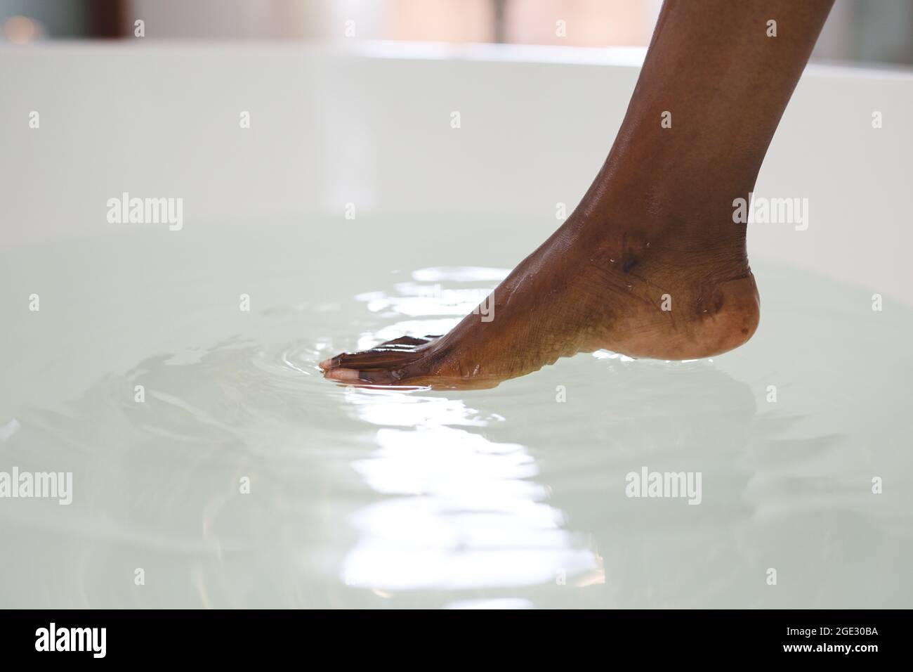 Primo piano di piede di donna afroamericana in bagno toccando acqua in bagno Foto Stock