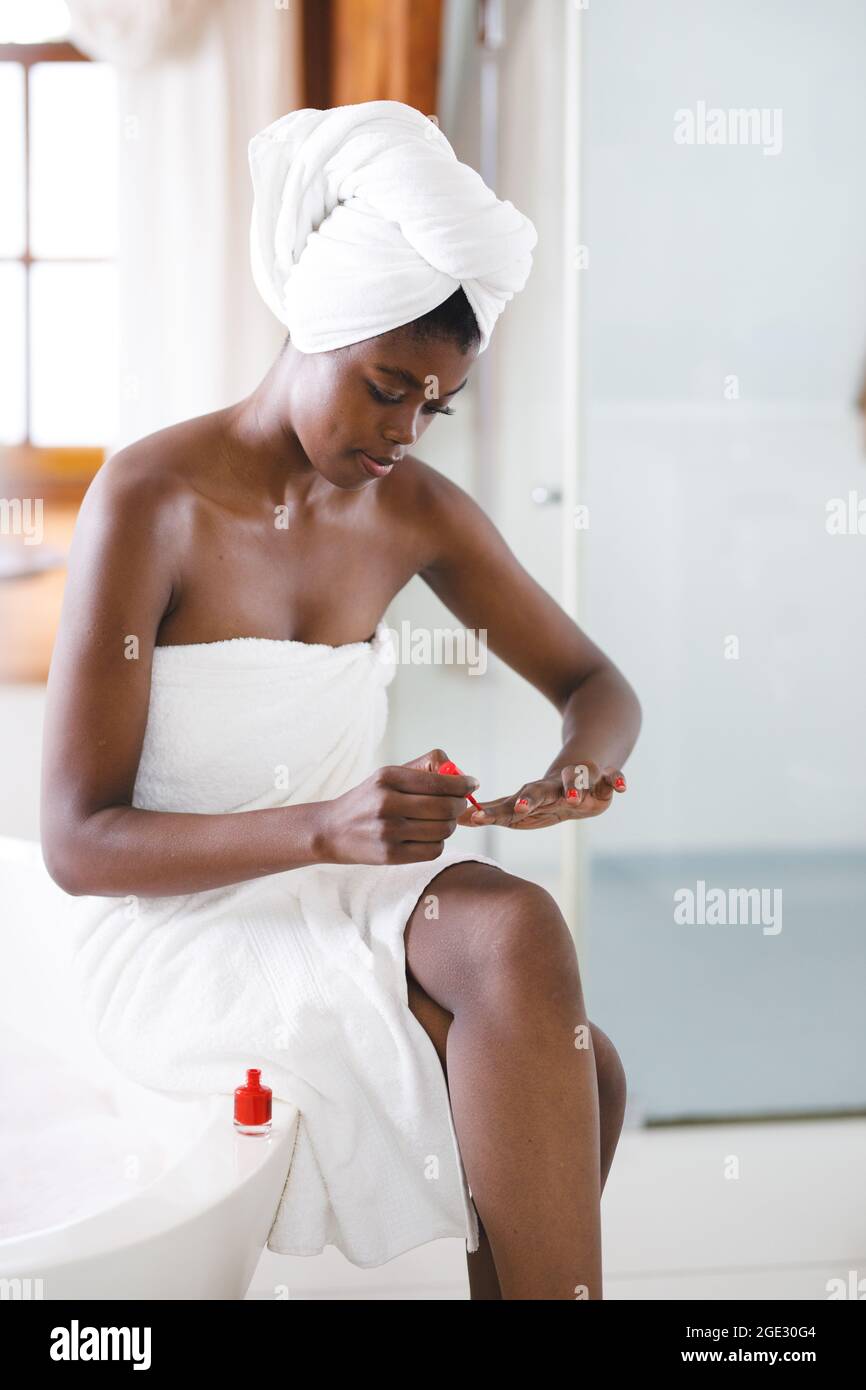 Sorridente donna afroamericana in bagno dipingendo le unghie con smalto rosso per unghie Foto Stock