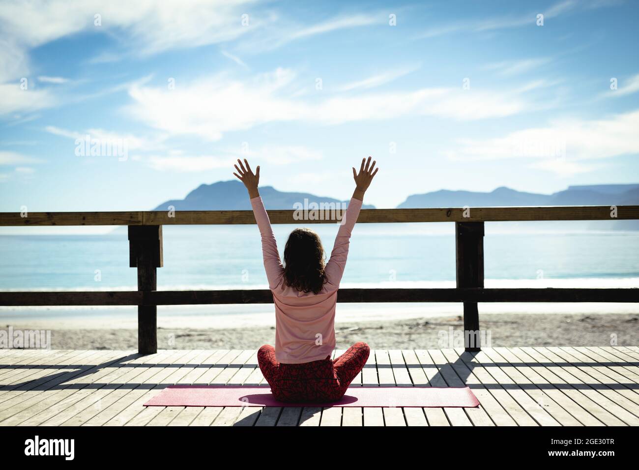 Donna da corsa mista che pratica yoga in giornata di sole al mare Foto Stock