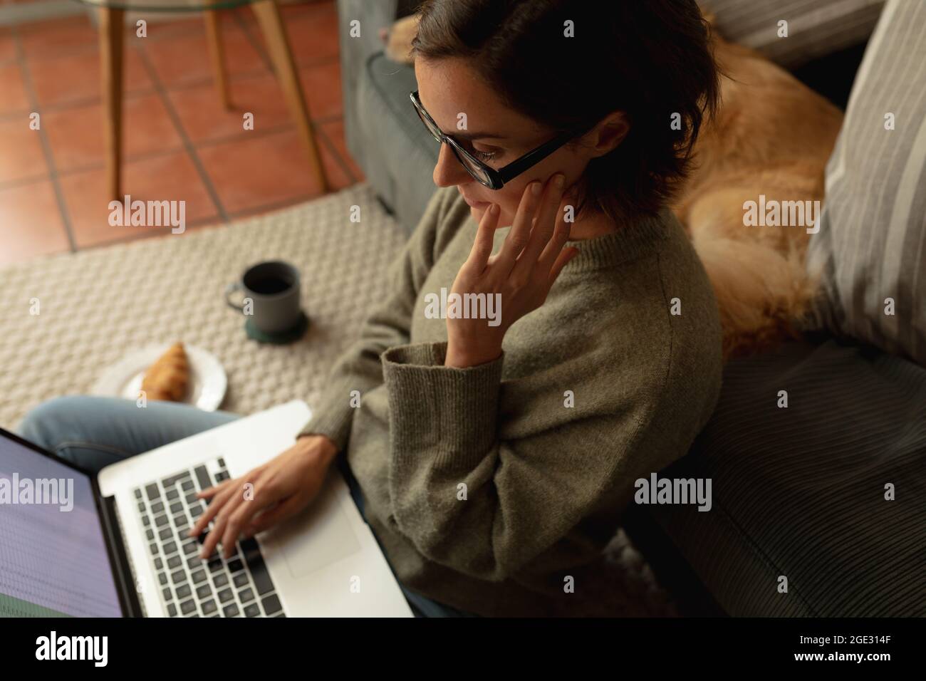 Donna caucasica in soggiorno con il suo cane da compagnia, seduta sul pavimento, lavoro con computer portatile Foto Stock