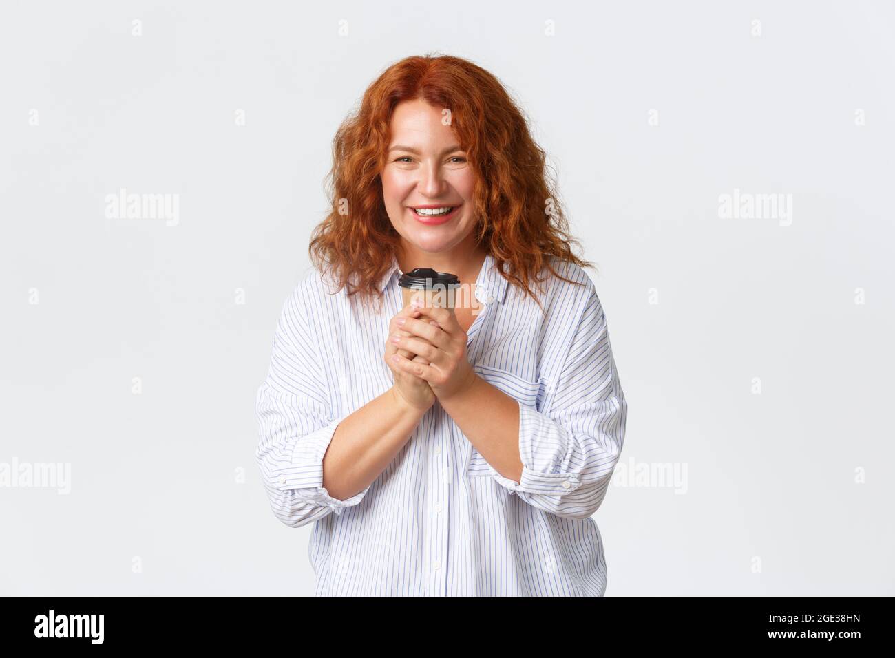 Emozioni, stile di vita e concetto di svago. Bella donna adulta rossa felice in blusa, tenendo una tazza di caffè da asporto e sorridendo gioiosa, godendosi Foto Stock