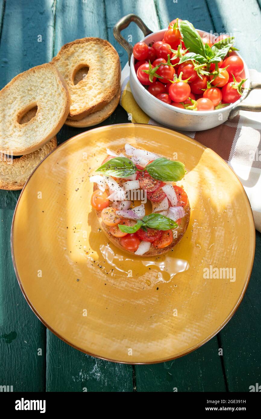 Rappresentazione fotografica del colorato e fresco piatto Friselle tipico della Puglia in Italia presentato in un piatto giallo Foto Stock