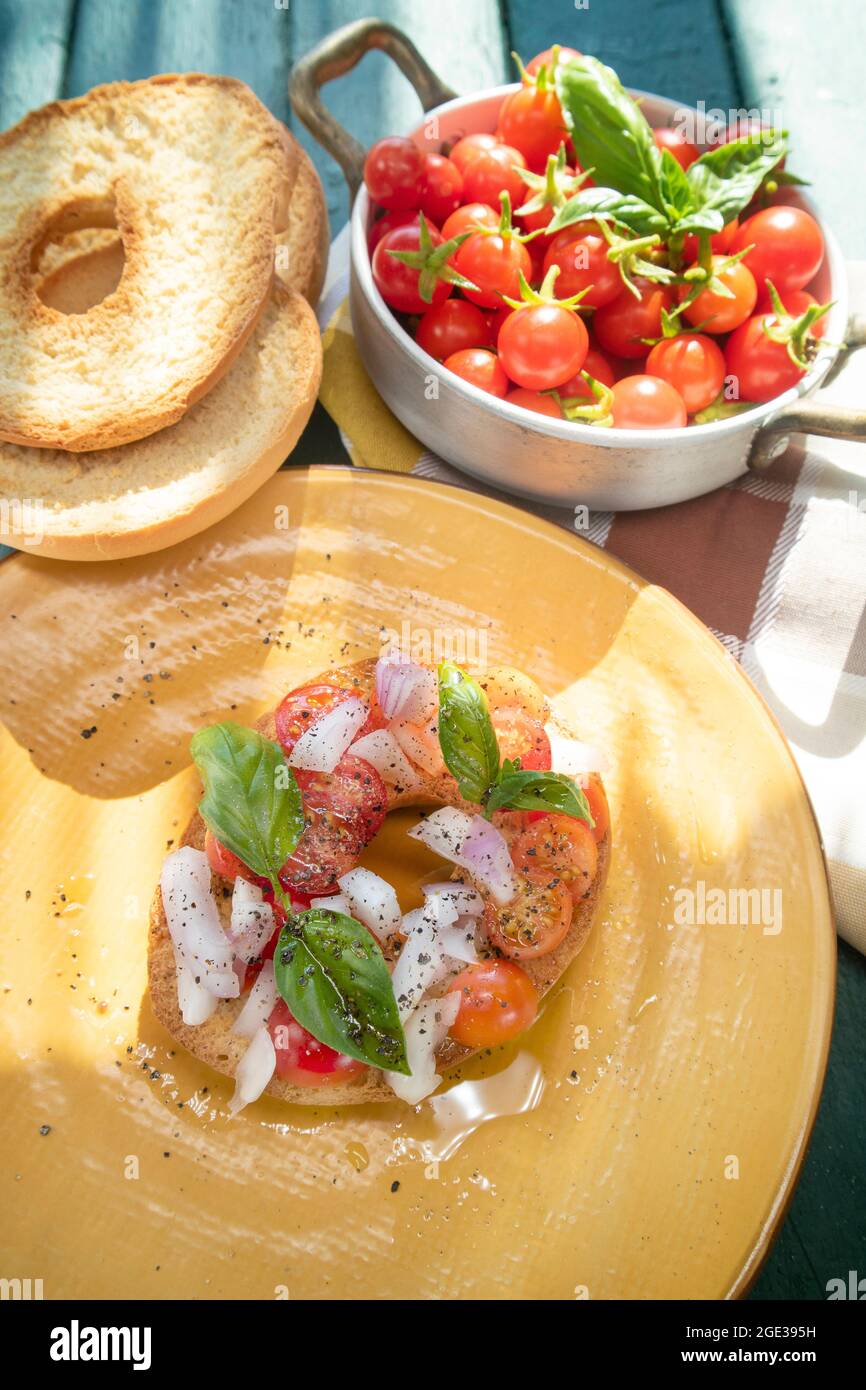 Rappresentazione fotografica del colorato e fresco piatto Friselle tipico della Puglia in Italia presentato in un piatto giallo Foto Stock