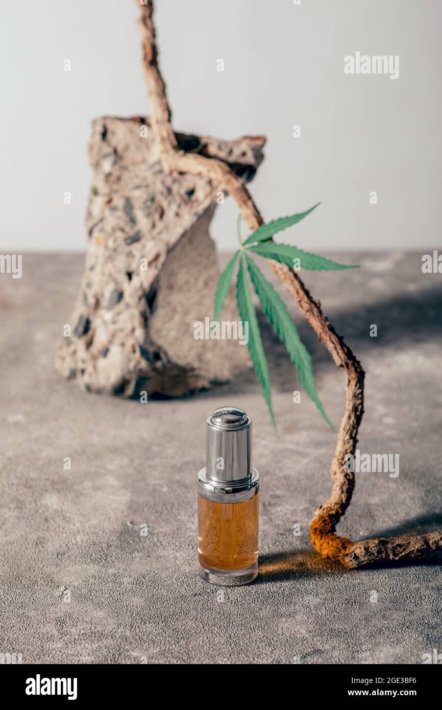 Bottiglia di vetro con olio CBD, tintura THC e foglia di canapa su sfondo di marmo grigio. Minimalismo, naturalezza. Cosmetici a olio CBD. Foto Stock