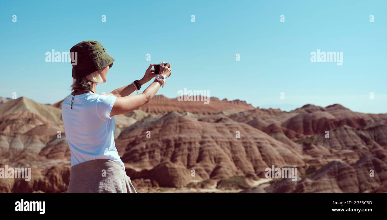 donna turistica asiatica scattando una foto delle terre yardang utilizzando il telefono cellulare nel parco geologico nazionale, vista posteriore Foto Stock