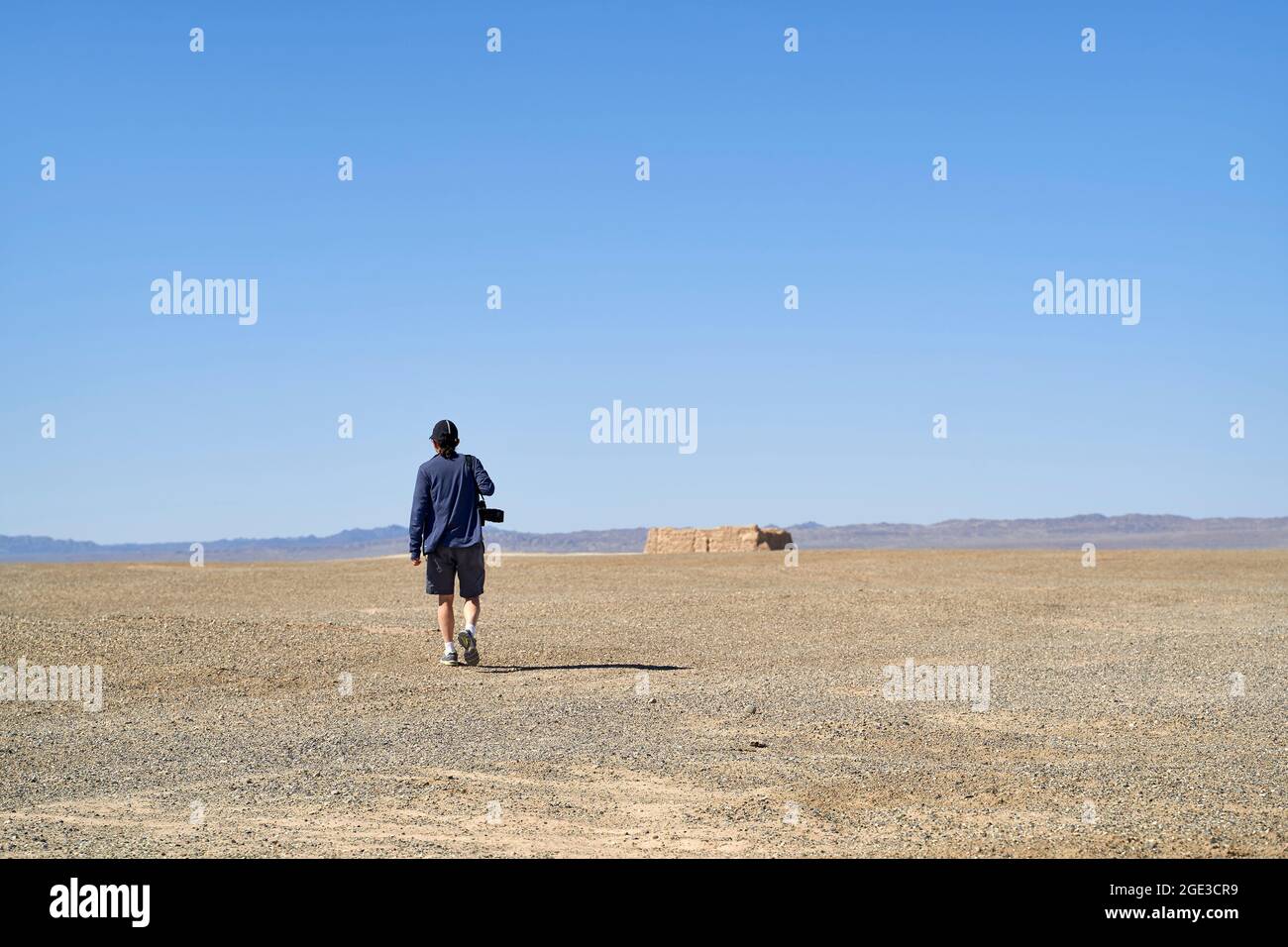 vista posteriore di un fotografo asiatico che cammina nel deserto di gobi sotto la telecamera con cielo blu Foto Stock