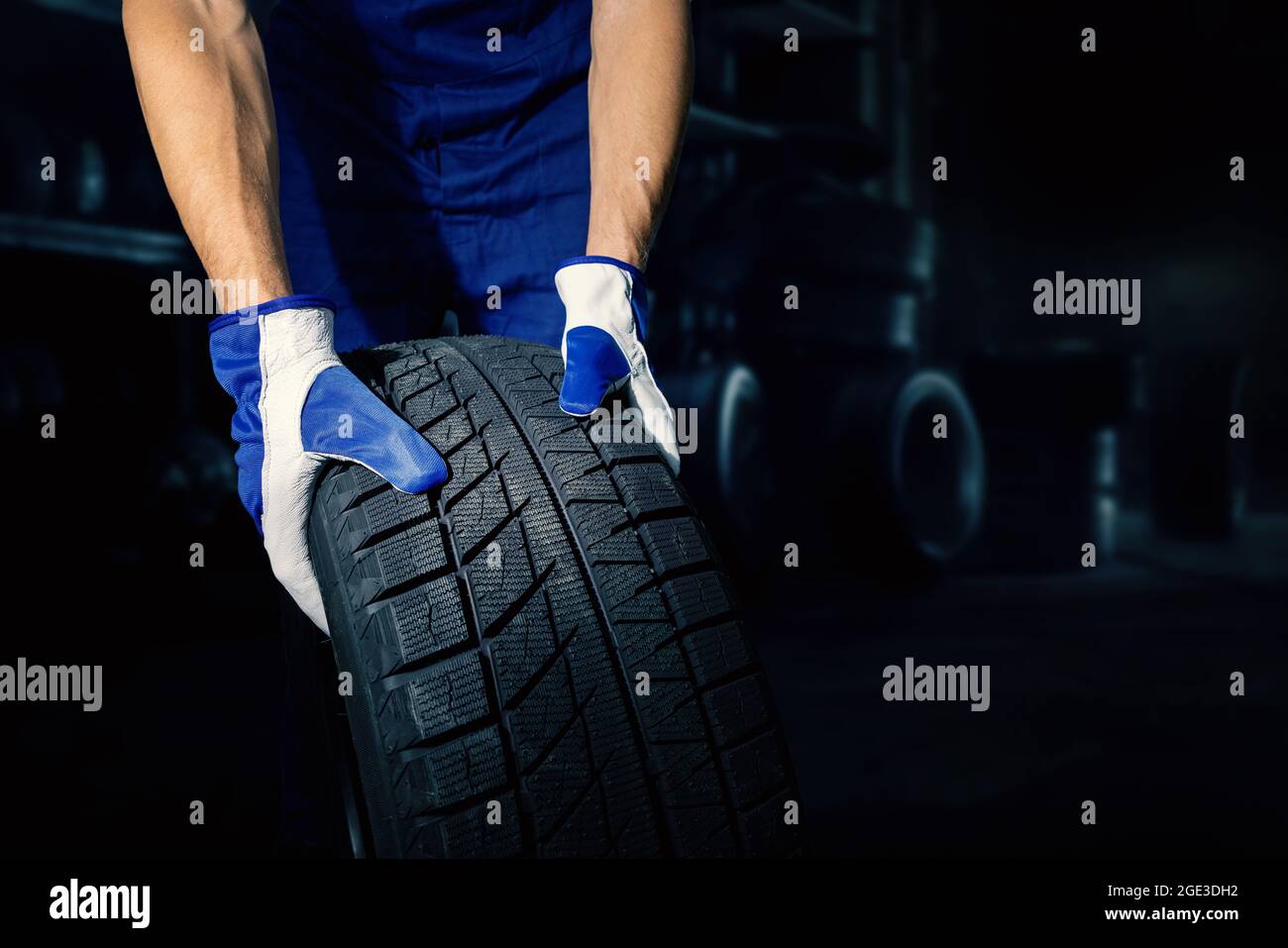 meccanico che tiene il pneumatico dell'auto su sfondo scuro dell'officina con spazio di copia. servizio pneumatici Foto Stock
