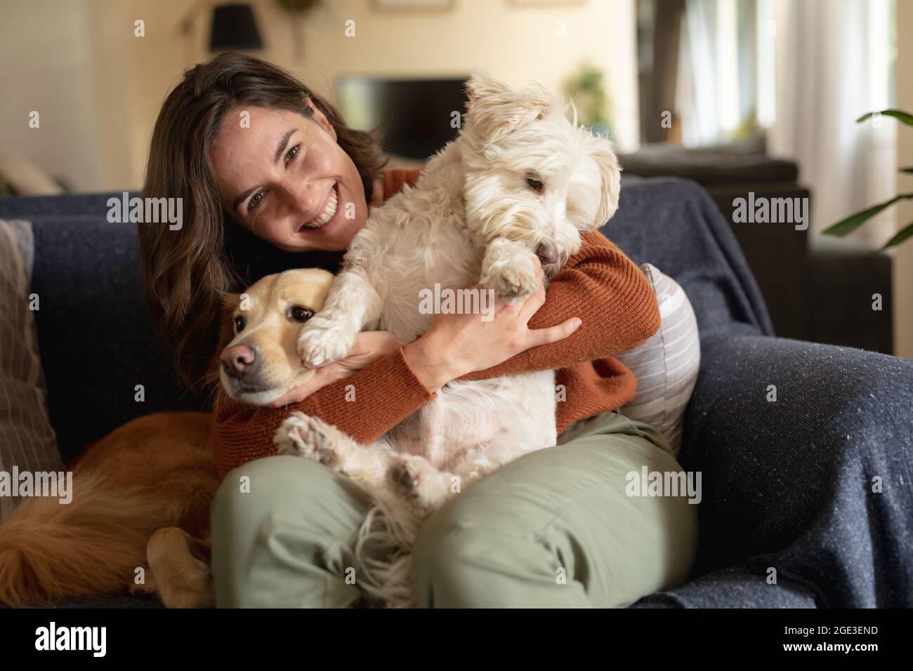 Ritratto di donna caucasica sorridente in soggiorno seduto sul divano che abbraccia i suoi cani da compagnia Foto Stock