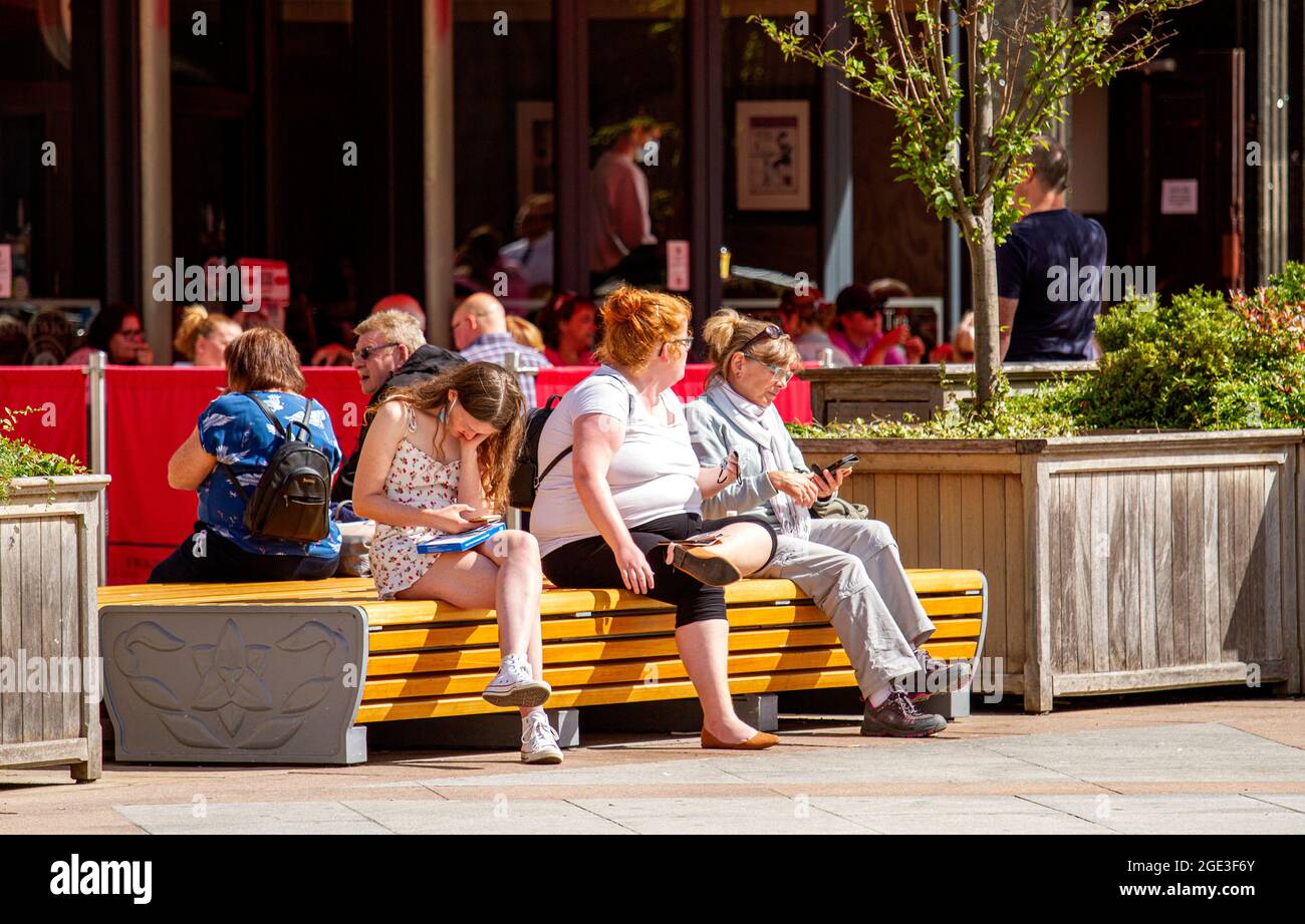 Dundee, Tayside, Scozia, Regno Unito. 16 agosto 2021. UK Meteo: Una calda giornata di sole con una leggera brezza fresca attraverso la Scozia Nord Est con temperature che raggiungono i 20°C. Una giovane donna seduta su un sedile che gode del caldo sole mentre invia messaggi di testo sul suo telefono cellulare e tiene un kit di auto-test Covid-19 nel centro di Dundee. Credit: Dundee Photographics/Alamy Live News Foto Stock