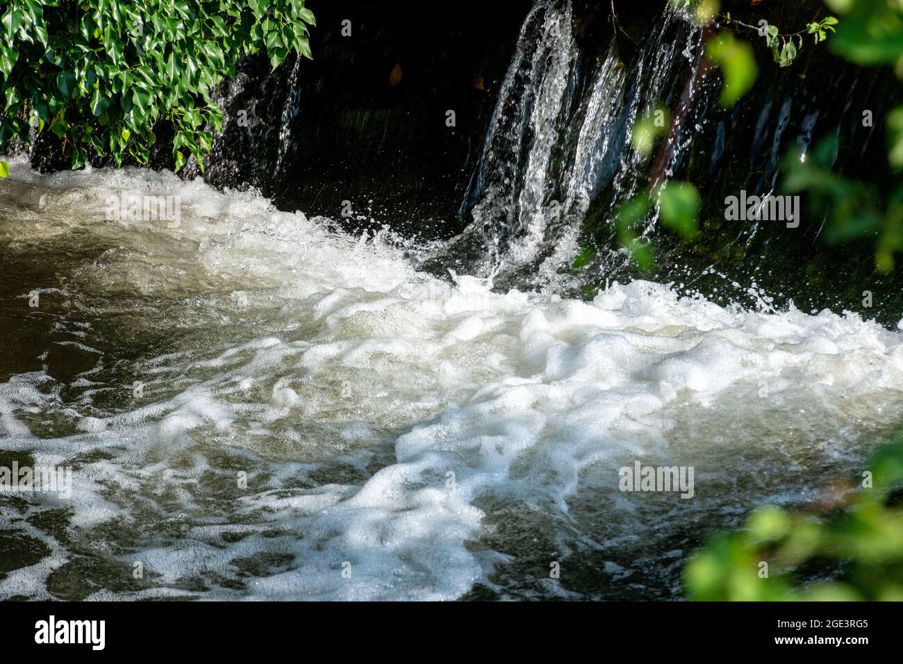 Acqua bianca alla base di un piccolo wier dove l'acqua cade sopra. Foto Stock