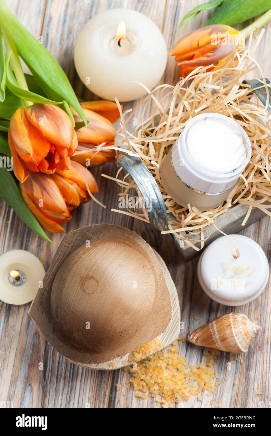 Sali da bagno e cosmetici arancioni su sfondo ligneo, candele accese e tulipani Foto Stock