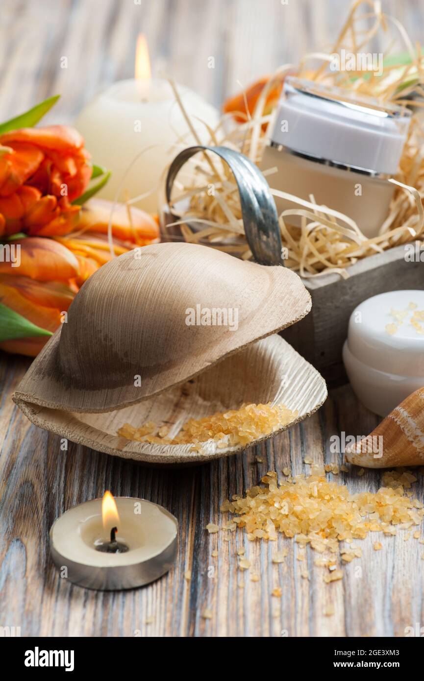 Sali da bagno e cosmetici arancioni su sfondo ligneo, candele accese e tulipani Foto Stock