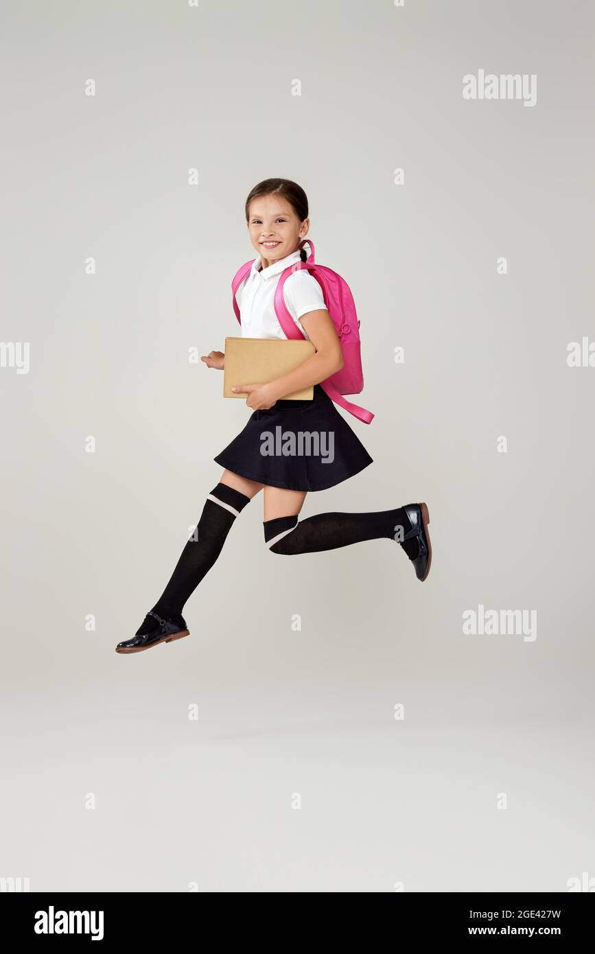 carina studentessa salta con zaino rosa isolato su sfondo grigio. felice bambino è pronto ad imparare. Ritorno a scuola Foto Stock