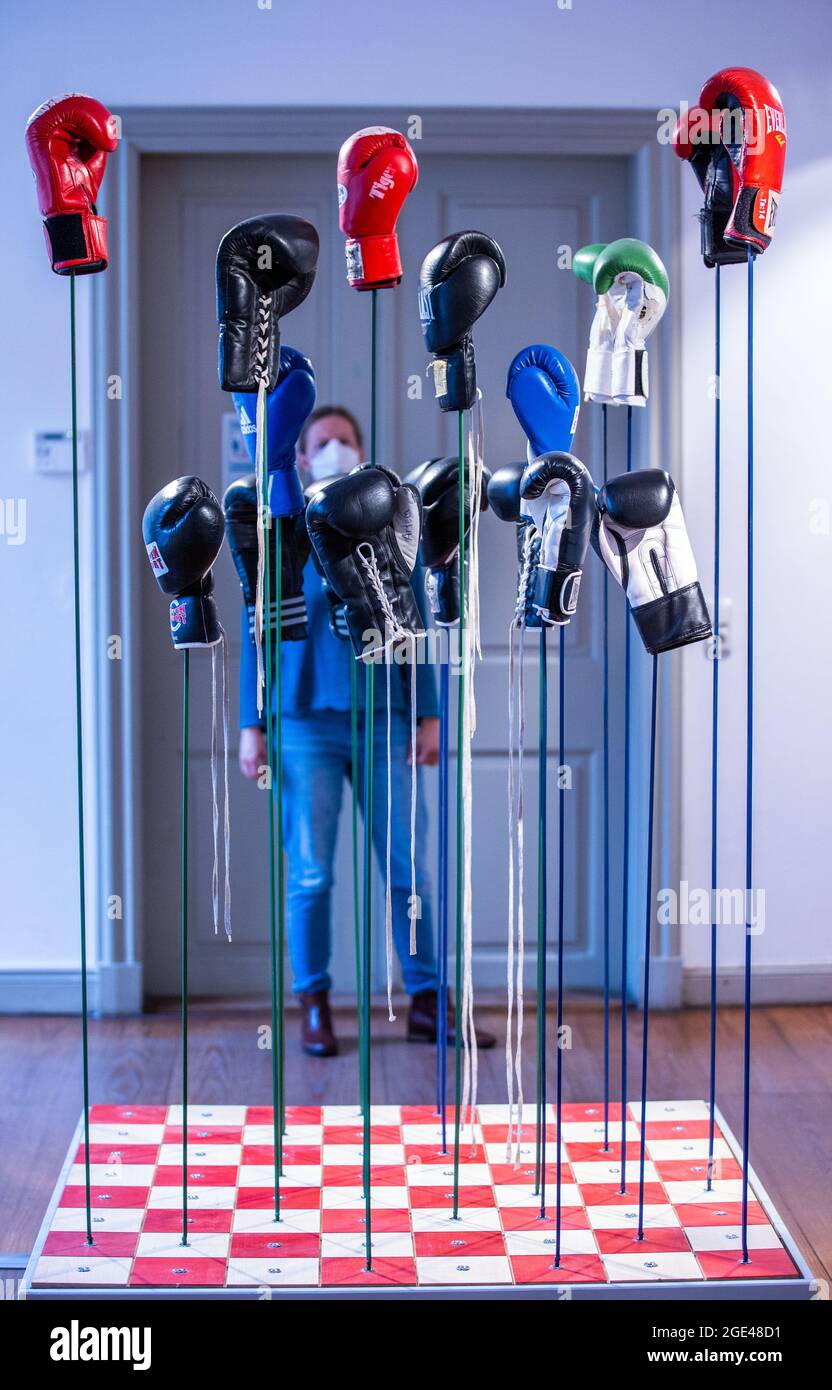 16 agosto 2021, Meclemburgo-Pomerania occidentale, Schwerin: Una donna si trova dietro l'installazione di "Agiles" di Stefan Nestler nella mostra speciale "Old Masters, Young Masters - Traktor Schwerin and the Art of Boxing" al Kulturforum Schleswig-Holstein-Haus. Foto, poster e registrazioni audio forniscono informazioni sul lavoro del club di boxe. Con numerose medaglie internazionali ai Campionati europei, ai Campionati del mondo, alla Coppa del mondo e alle Olimpiadi, oltre a 17 titoli come campioni del team GDR e 86 campioni senior della GDR, i pugili della SC Traktor hanno dominato il mondo della boxe nella Foto Stock