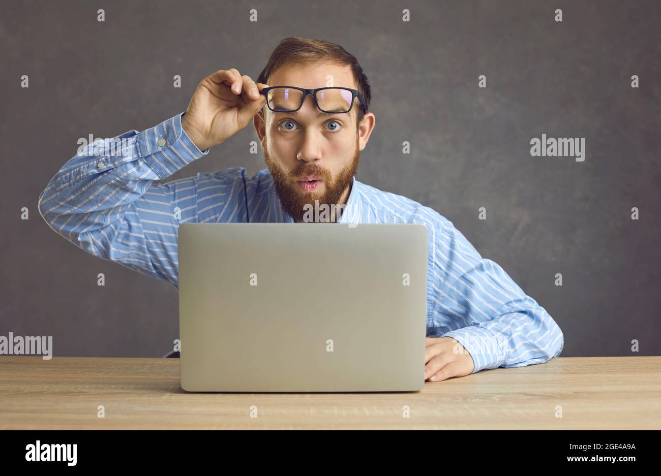 Il lavoratore sorpreso toglie gli occhiali e guarda qualcosa di scioccante che accade in ufficio Foto Stock