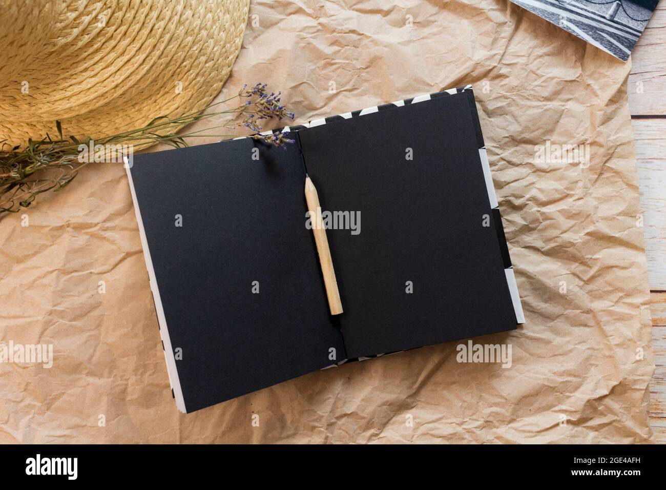 Composizione piatta con un taccuino nero vuoto aperto, matita, cartolina bianco-nero, lavanda secca e cappello di paglia su fondo di carta artigianale. Vista dall'alto. Foto Stock