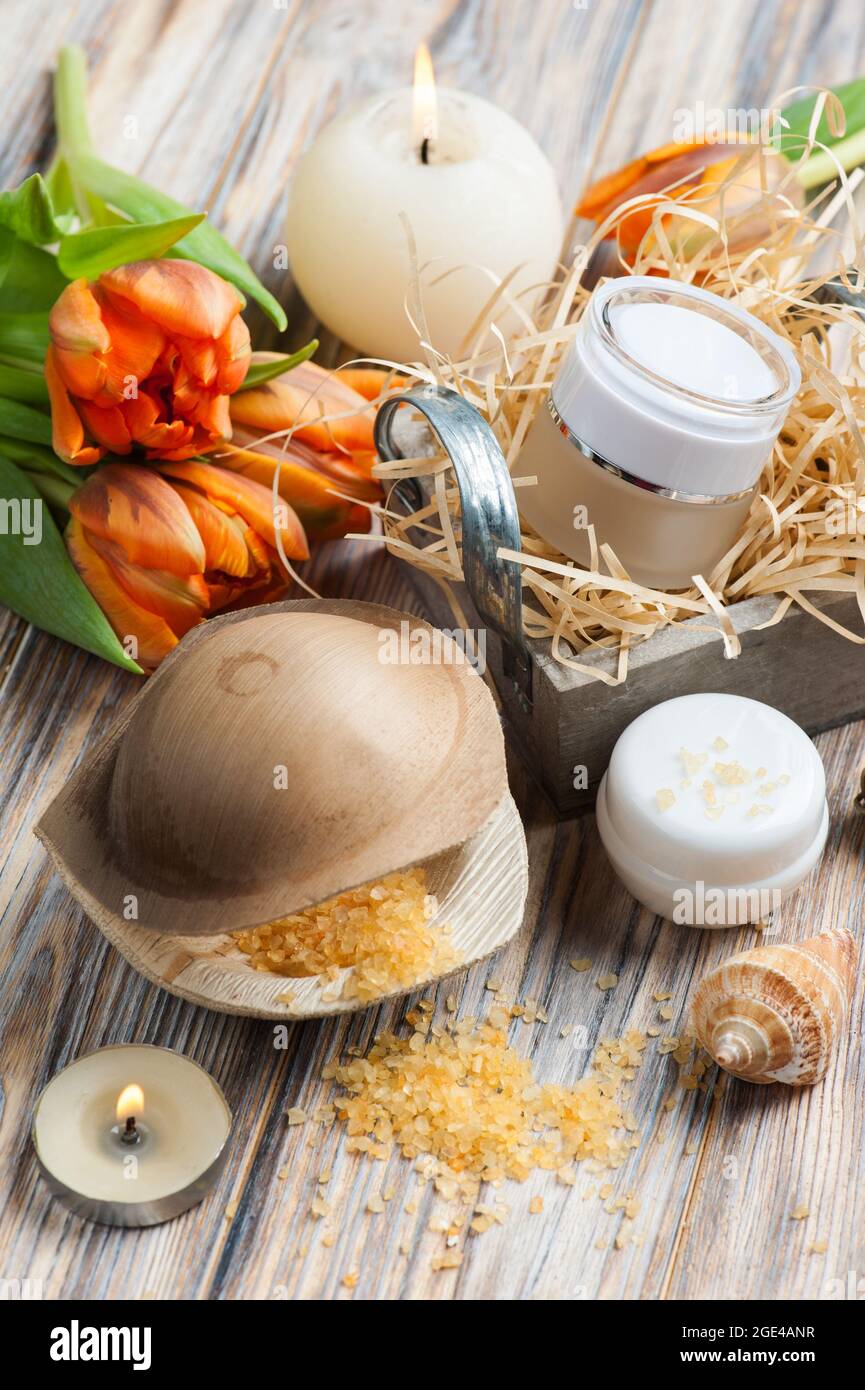 Sali da bagno e cosmetici arancioni su sfondo ligneo, candele accese e tulipani Foto Stock