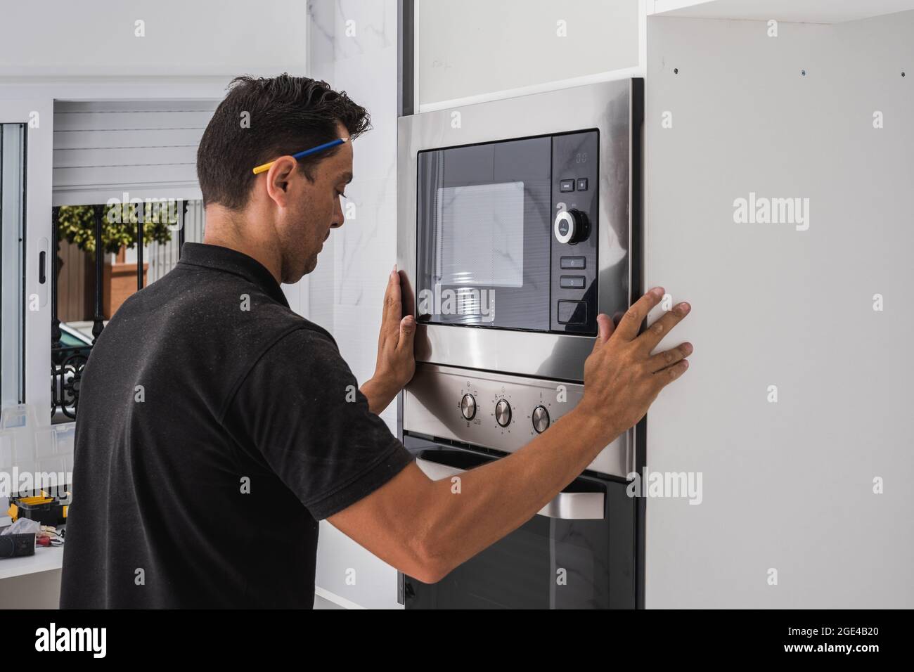 Uomo che monta un forno a microonde all'interno del foro di un nuovo mobile da cucina Foto Stock