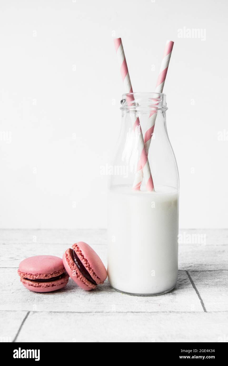 Piccola bottiglia di latte in vetro con cannucce di carta a strisce di caramelle rosa e macaron rosa Foto Stock