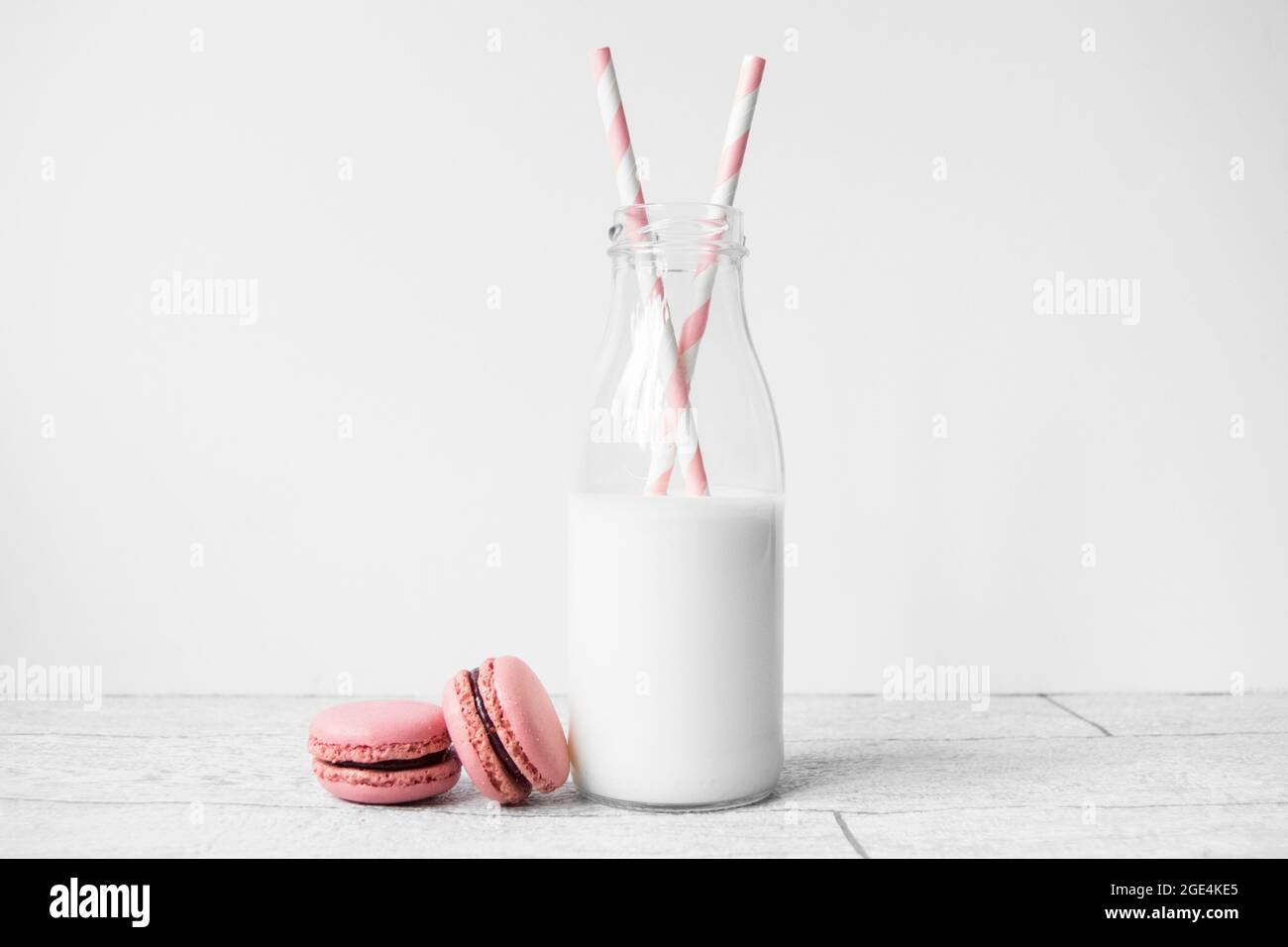 Piccola bottiglia di latte in vetro con cannucce di carta a strisce di caramelle rosa e macaron rosa Foto Stock